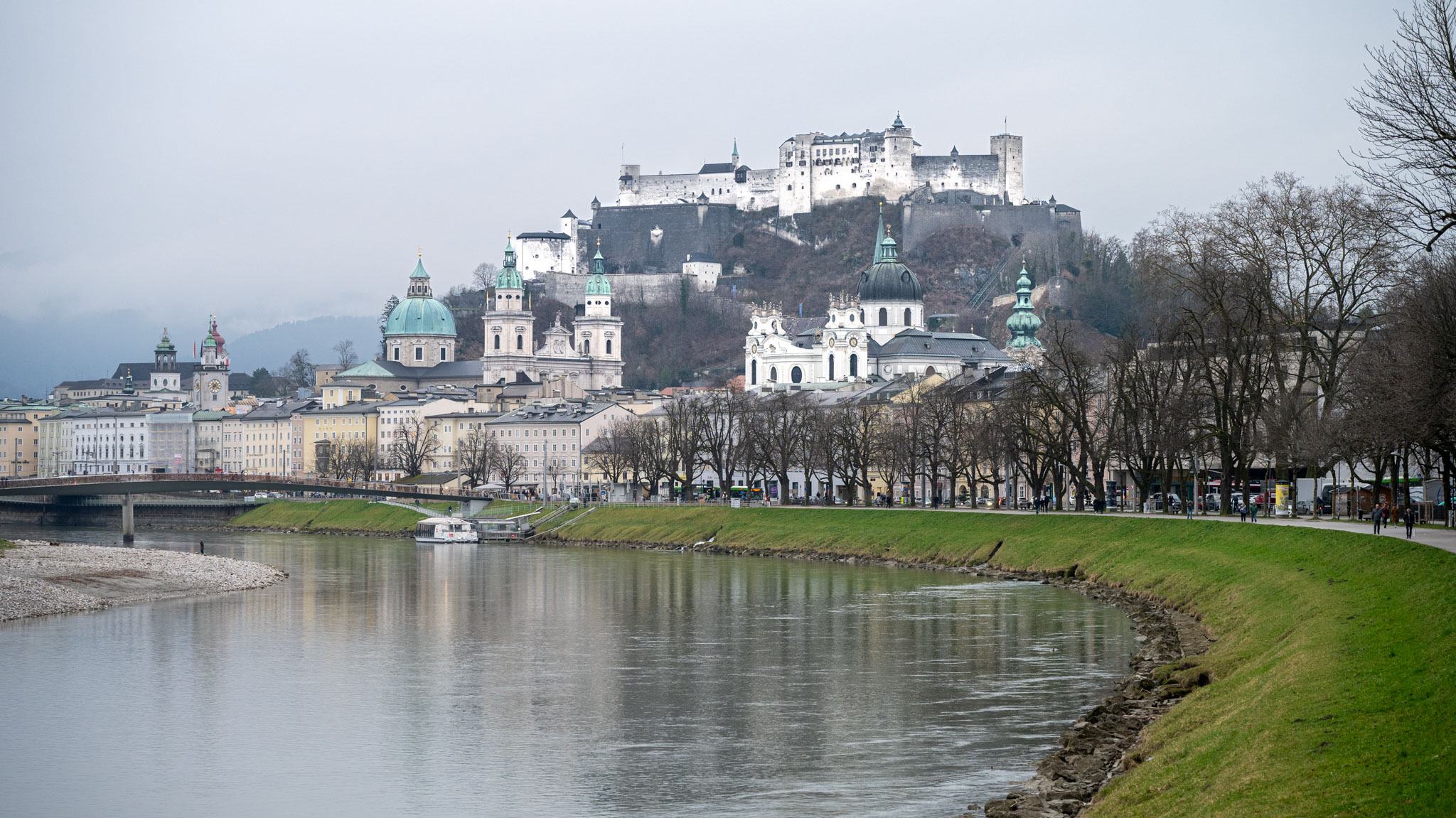 Blick vom Ufer der Salzach auf die historische Altstadt von Salzburg und darüber die Festung Hohensalzburg